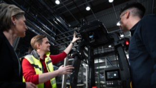 Three people are standing in front of an automated vehicle from Linde MH.