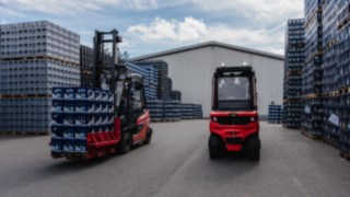 The Linde Reverse Assist Radar recognises every obstacle, regardless of lighting conditions. Two Linde electric forklift trucks are parked between stacks of crates in an outdoor premises.