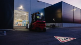 A forklift truck drives towards the roll-up door of a hall at dusk.