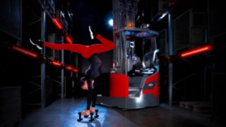 Acrobat performing a handstand next to the Linde MH reach truck Ri16 in a warehouse.