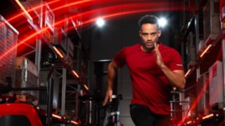 Athlete running in a warehouse with the Linde MH reach truck Ri16 in the background.